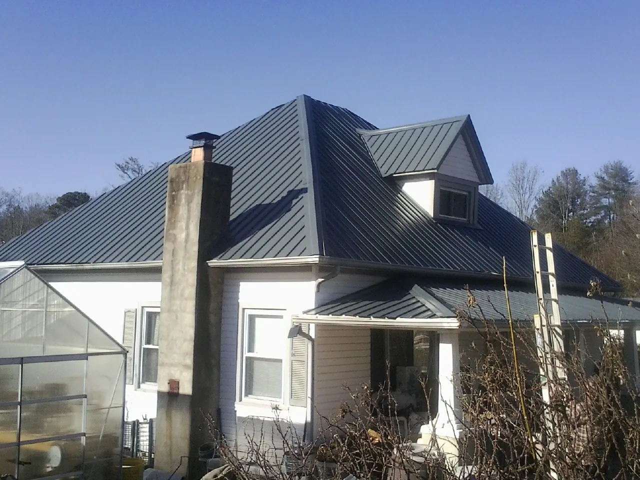 Dark blue standing seam metal roof on a white farmhouse with dormer — Slate & Tile Roof Repair by Roofing Brothers in Luling