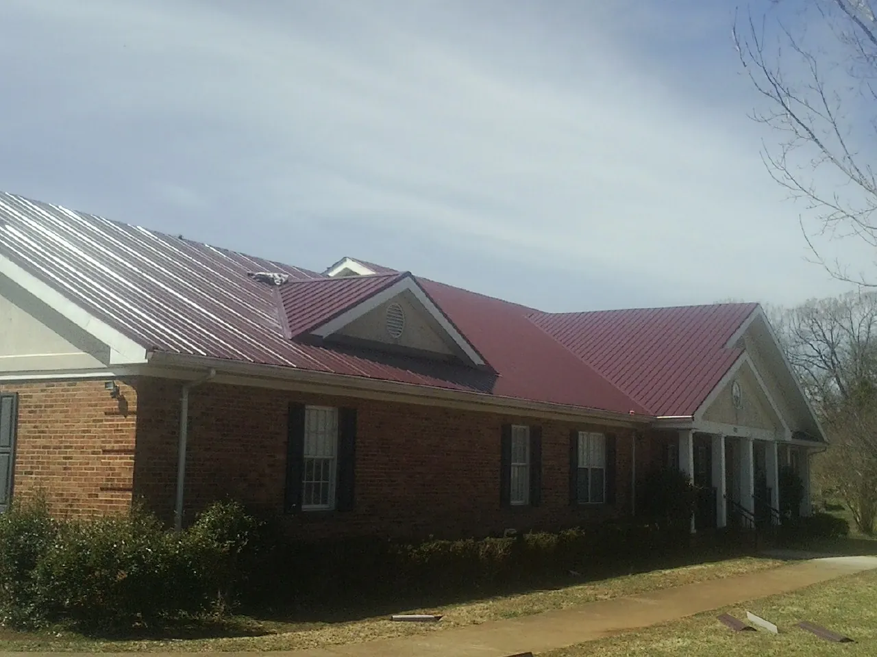 Red metal roof with gabled entries on a long brick building, from a Hail Damage Roof Repair job in Luling