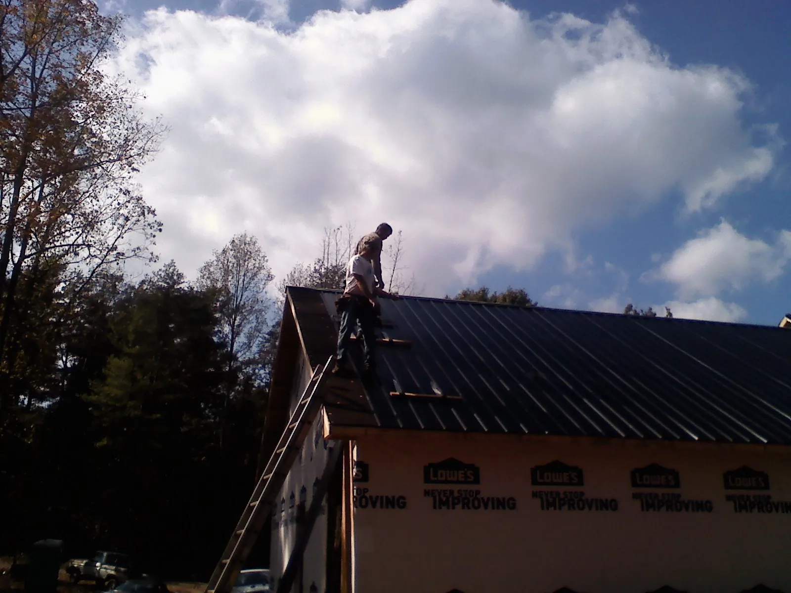 Roofer fastening dark metal panels high against a cloudy sky, from a Roof Inspection job in Luling