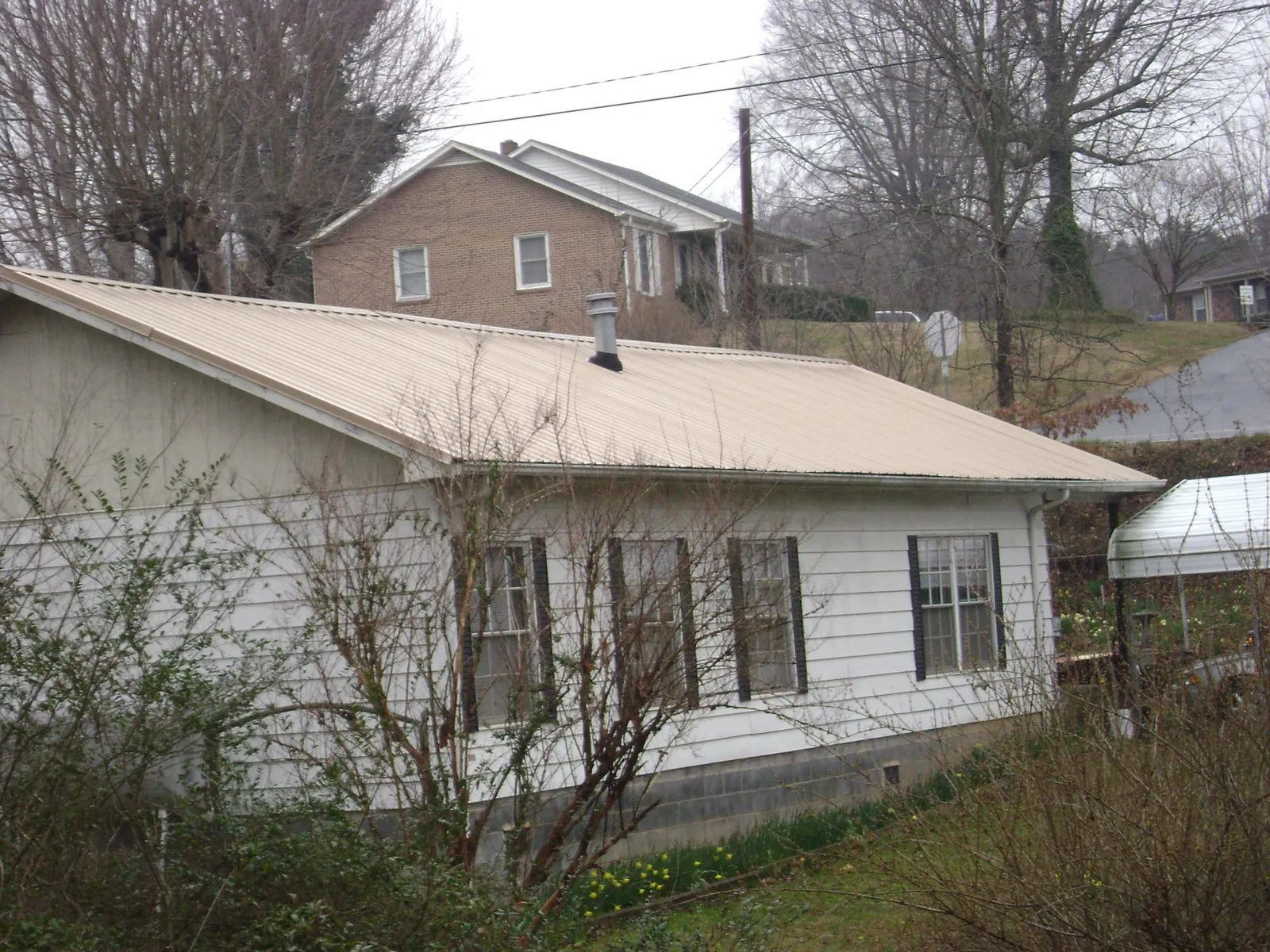Tan metal roof on a white sided house set into a hillside — Commercial Roofing by Roofing Brothers in Luling
